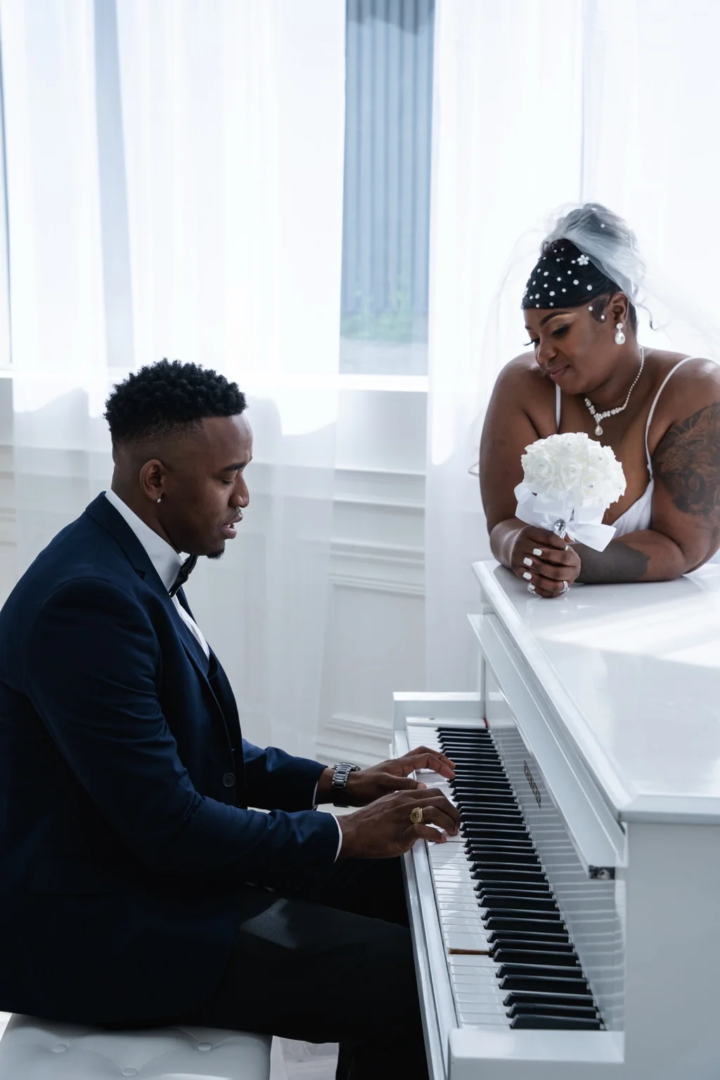 Groom playing a white piano while the bride looks on