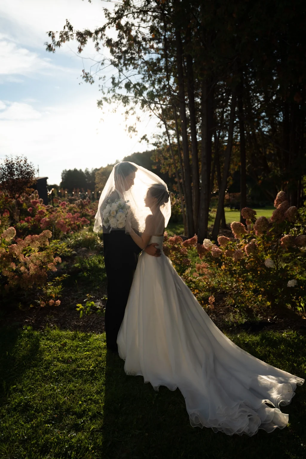 Silvia and Jerry photographed in a garden with evening light glowing through the bride’s veil